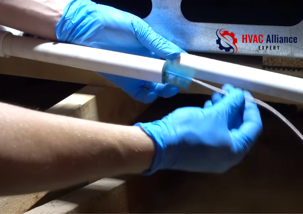 Technician cleaning AC drain trap in attic by inserting brush into PVC condensate drain line