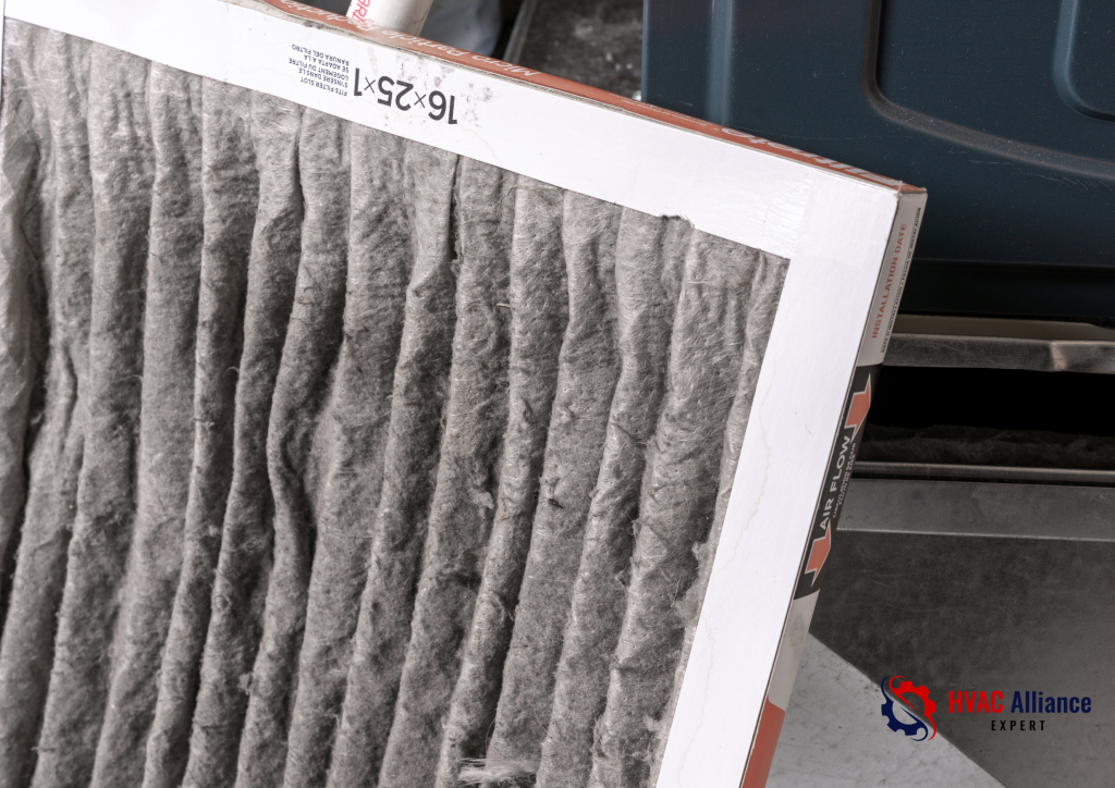 A close-up of a heavily clogged and dirty 16x25x1 HVAC air filter covered in a thick layer of grey dust, shown being removed from a furnace by an HVAC Alliance Expert.