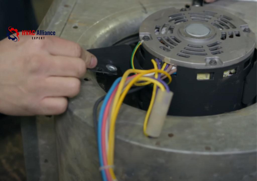 An HVAC technician's hands disassembling a furnace blower motor from its metal housing on a workbench for repair or replacement.